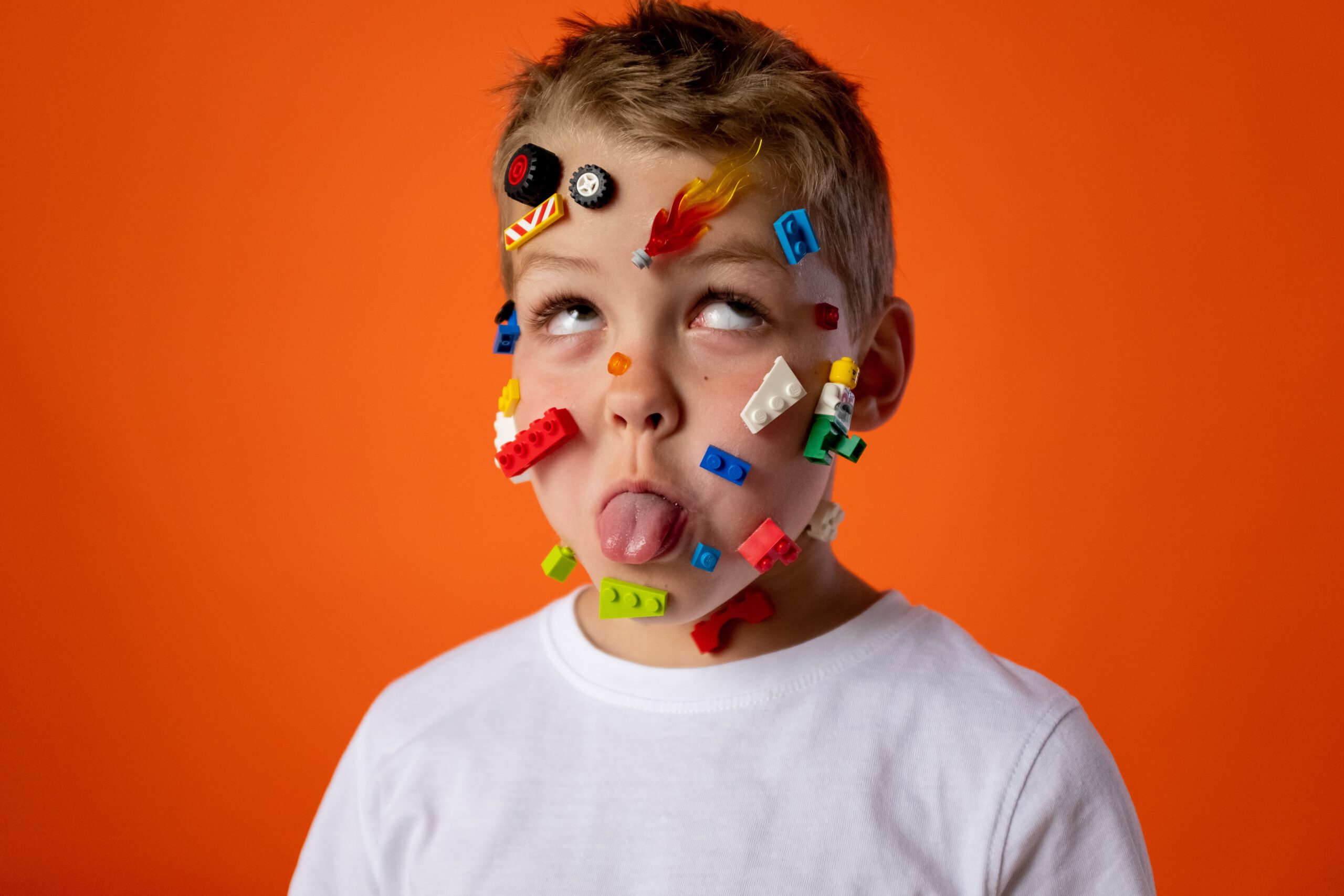 Chłopczyk z elementami klocków LEGO przyklejonymi na twarzy i ze śmieszną miną