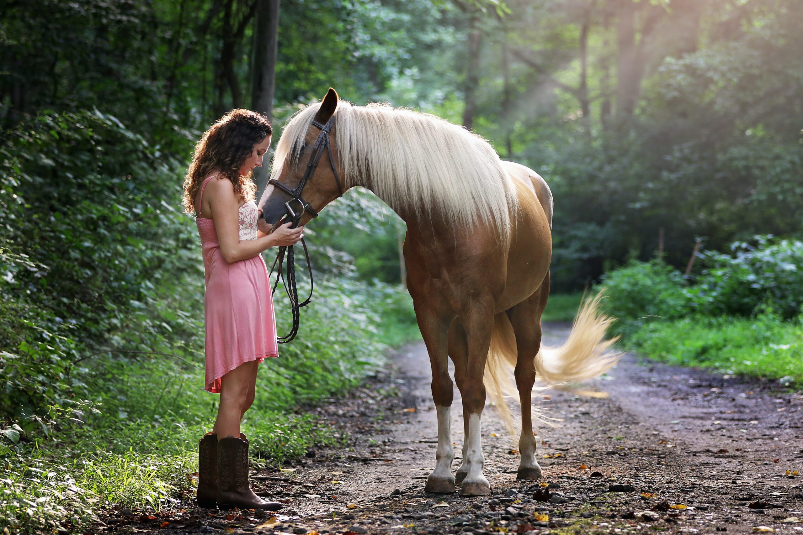 Młoda kobieta i brązowy koń stojący na leśniej dróżce