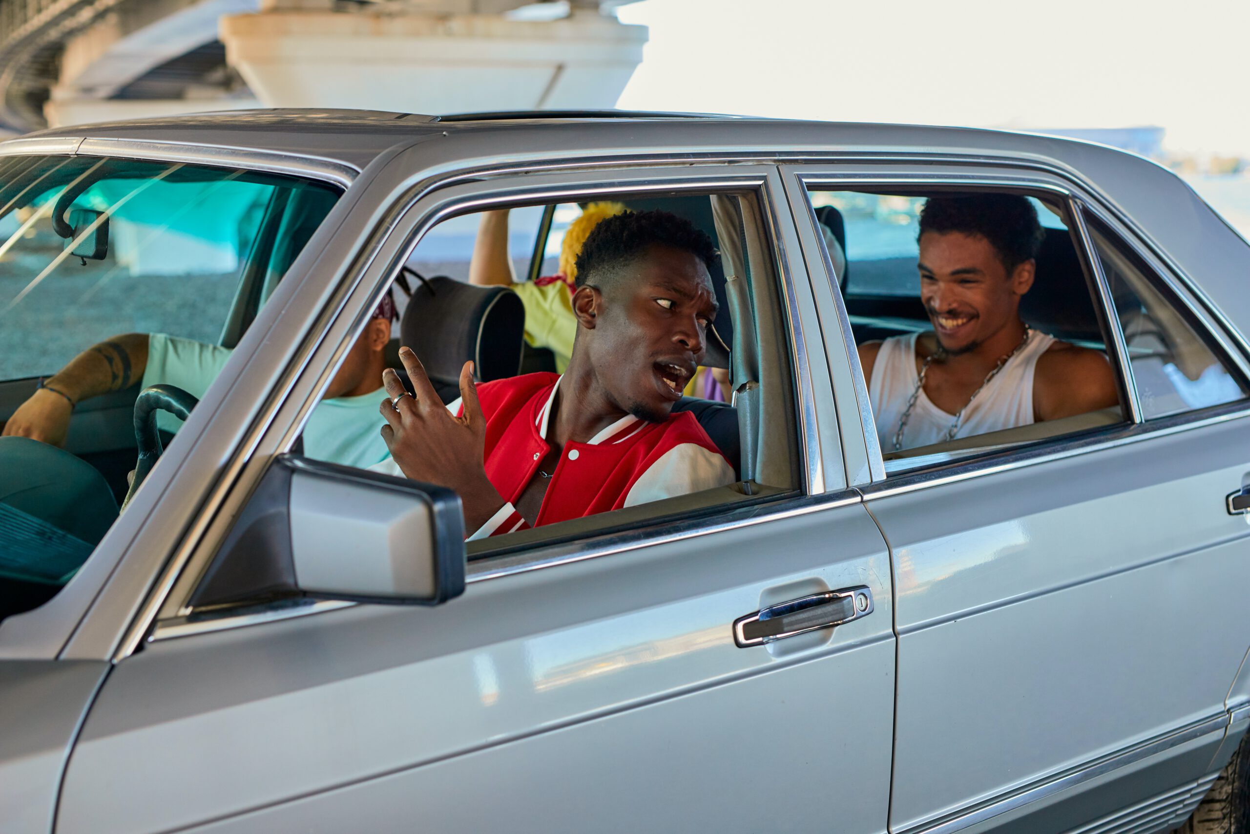 Nastolatkowie siedzący i śmiejący się do siebie w starym srebrnym samochodzie