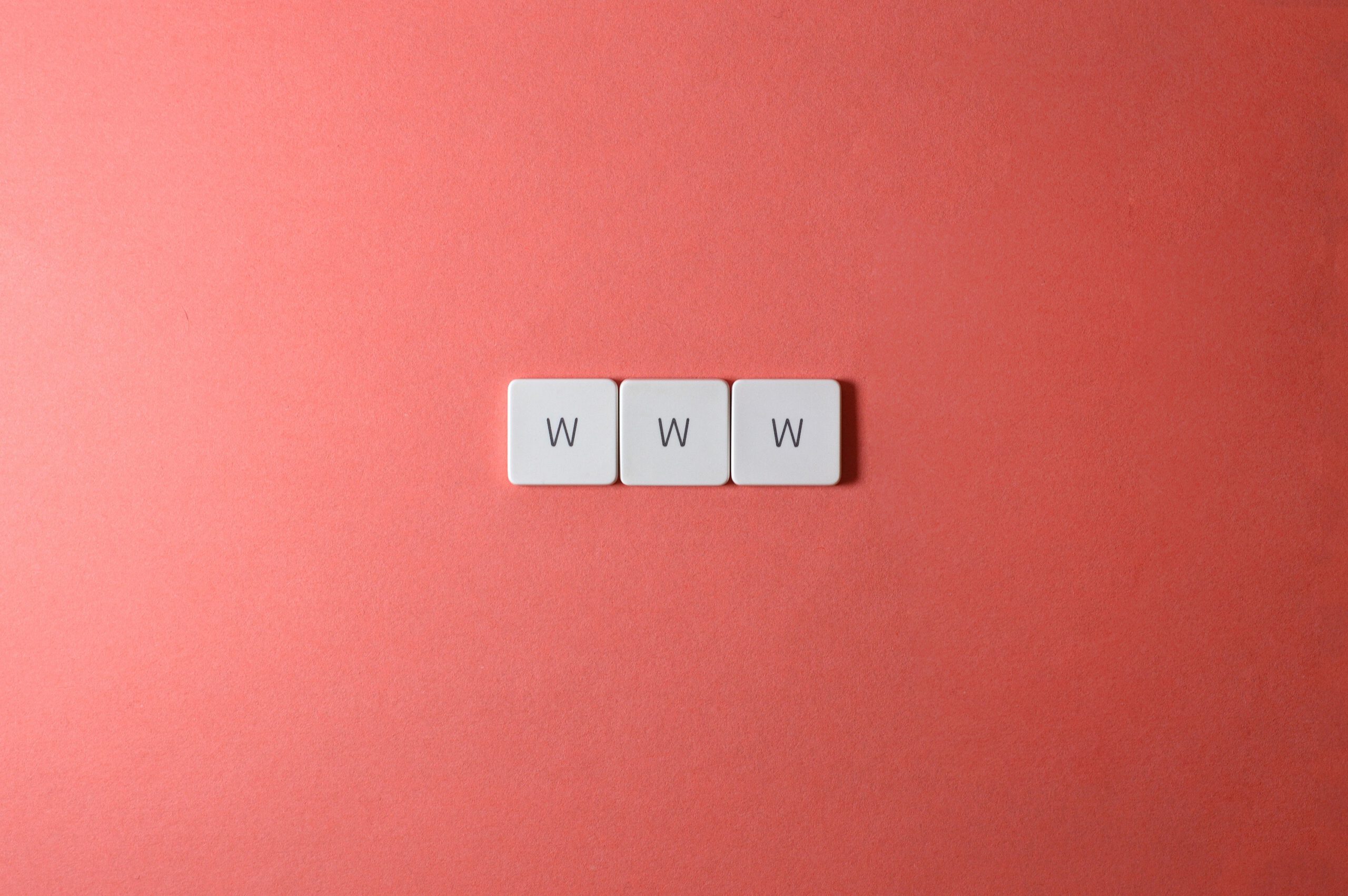 Trzy literki "w" na drewnianych kostkach, tworząe słowo "www" na czerwonym tle