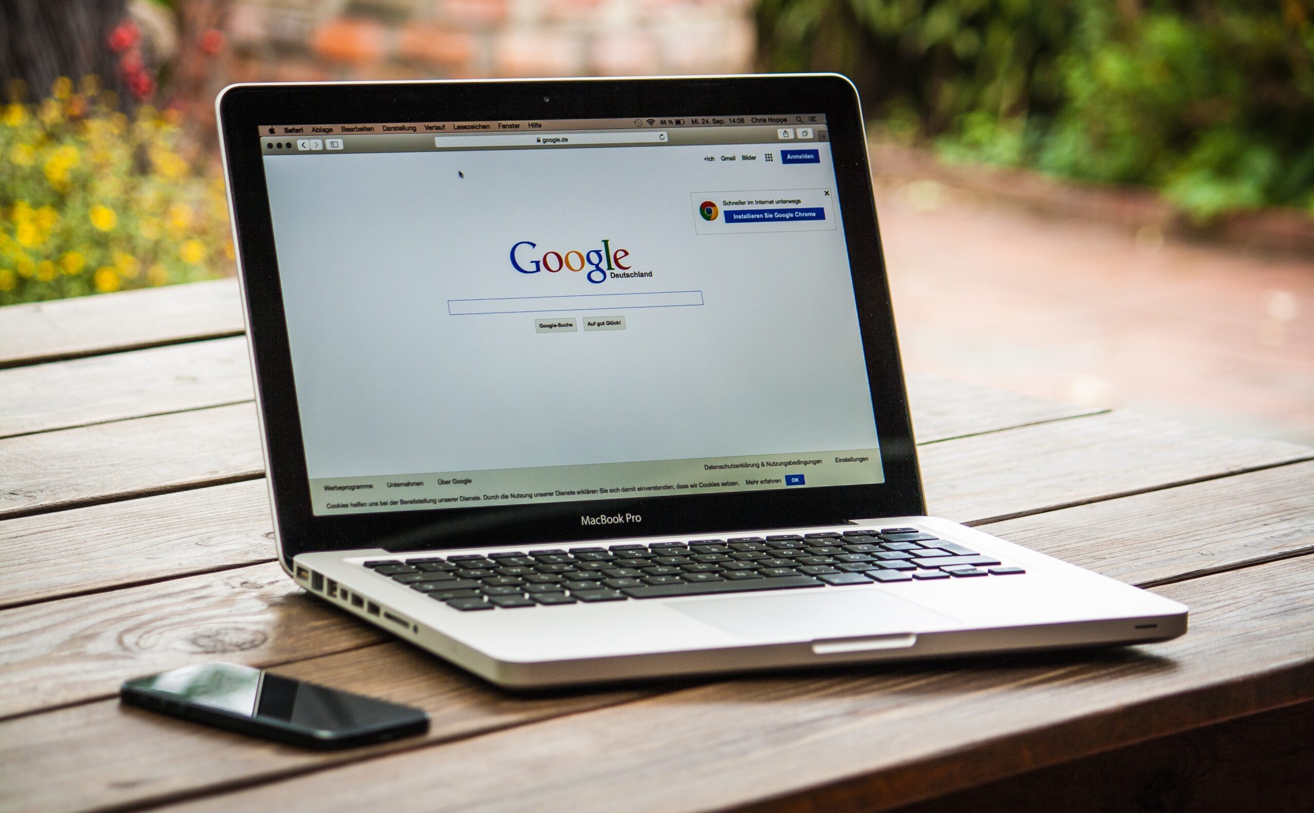 Wyszukiwarka Google otwarta na laptopie stojącym na drewnianym stole na zewnątrz